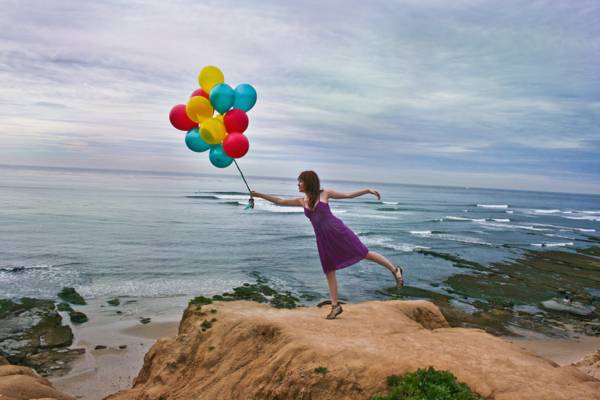 女人站在岩石的悬崖上,拿着气球高清壁纸