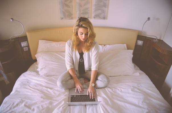 白色开放羊毛衫的女人坐在拿着MacBook Pro高清壁纸的白色床罩上