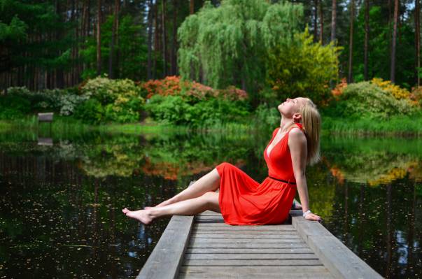 女人穿着红色的裙子,坐在灰色的木制湖码头高清壁纸