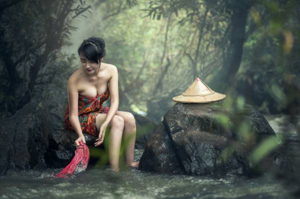 女人穿着黑色,棕色和绿色花毛巾坐在岩石上洗衣服在河里的高清壁纸