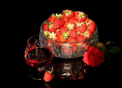 一杯草莓利口酒与成熟的草莓和一朵红玫瑰的桌子上