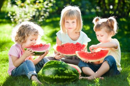 夏天，三个小女孩在绿草地上吃西瓜