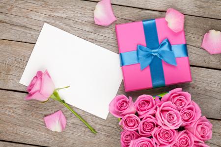 带着一束粉红色的玫瑰和一张纸桌上的礼物盒