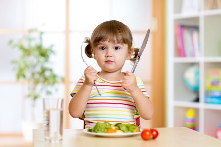 一个小女孩与餐具和一盘