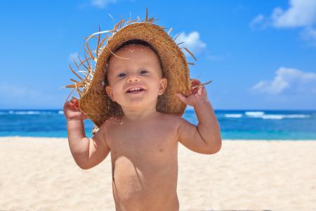 一顶草帽在海滩上的小微笑男孩