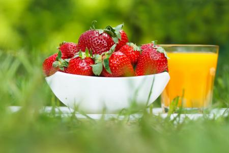 成熟的草莓和一杯橙汁在绿色草地上