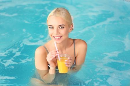 在一杯橙汁微笑金发女郎在游泳池