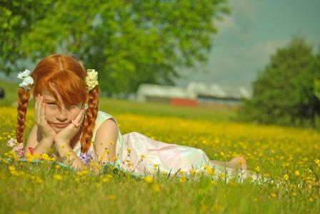 带着辫子的红发女孩躺在绿草地上